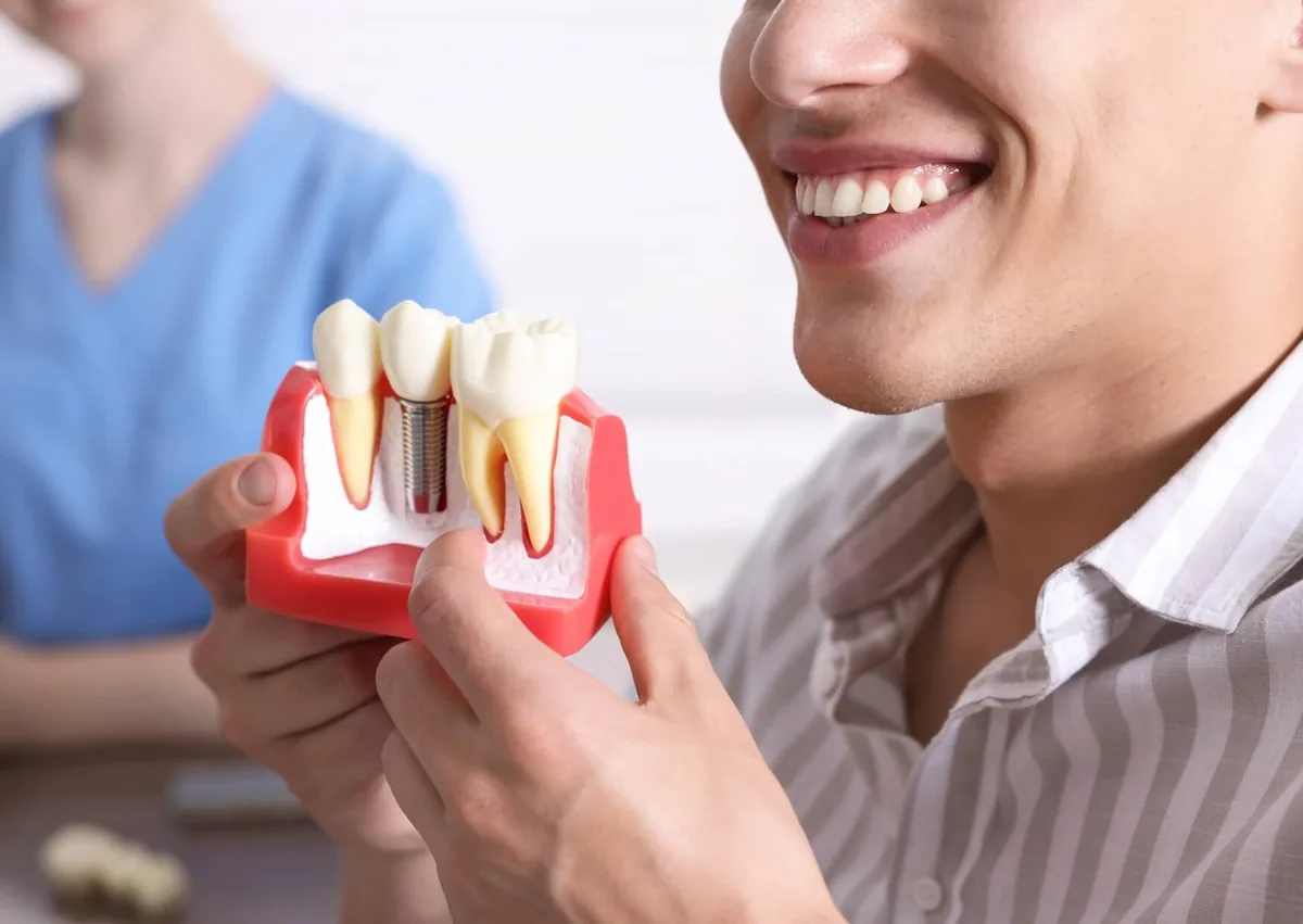 Patient holding a dental implant model showing how an implant replaces a missing tooth.