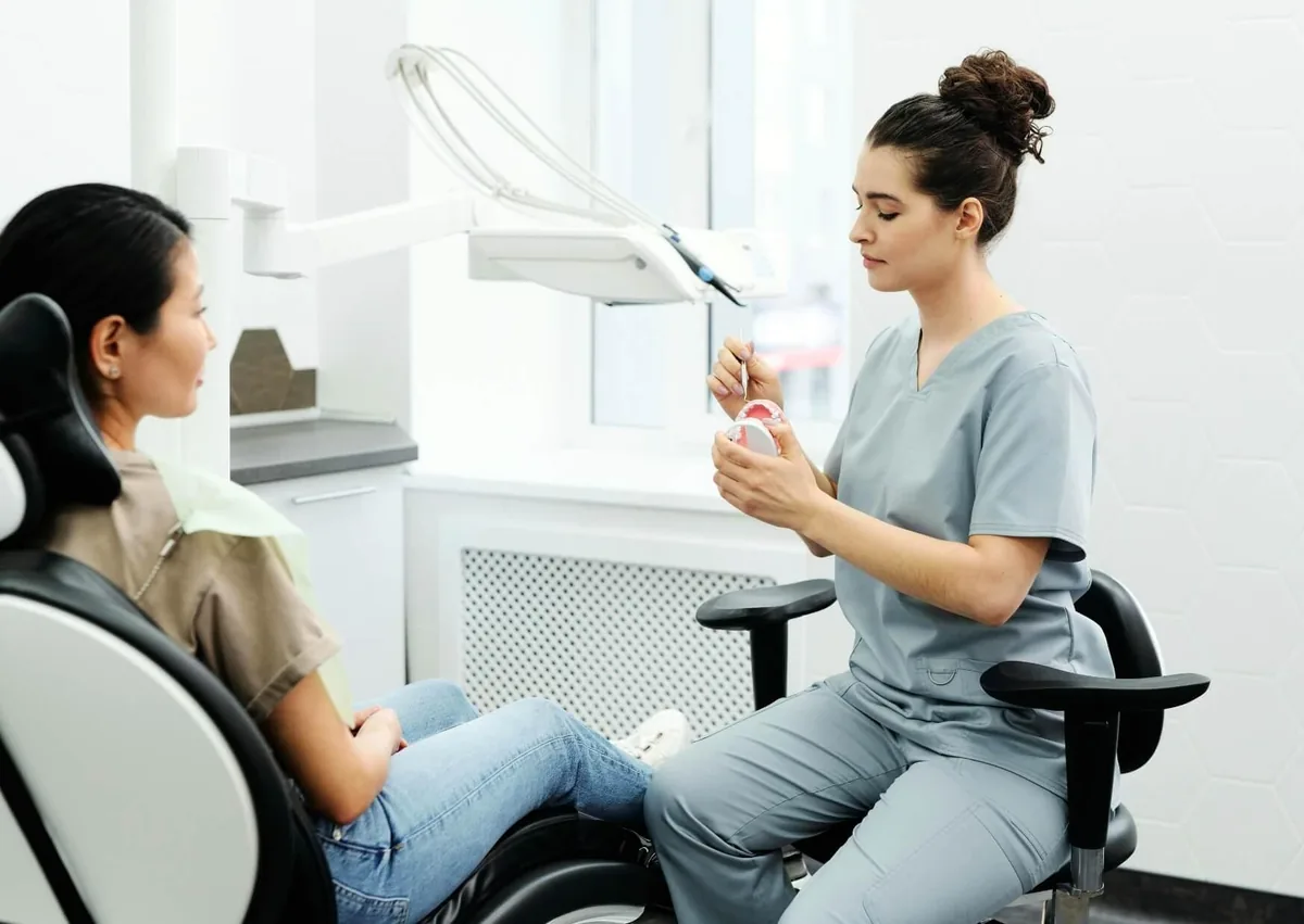 Dental professional explaining the tooth implant timeline to a patient using a dental model.