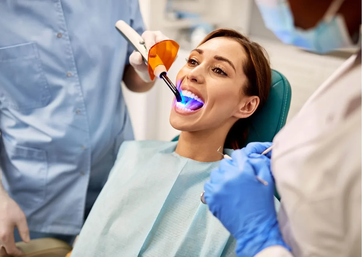 Dentist applying a blue curing light to a patient's teeth during a dental bonding procedure to improve tooth appearance.